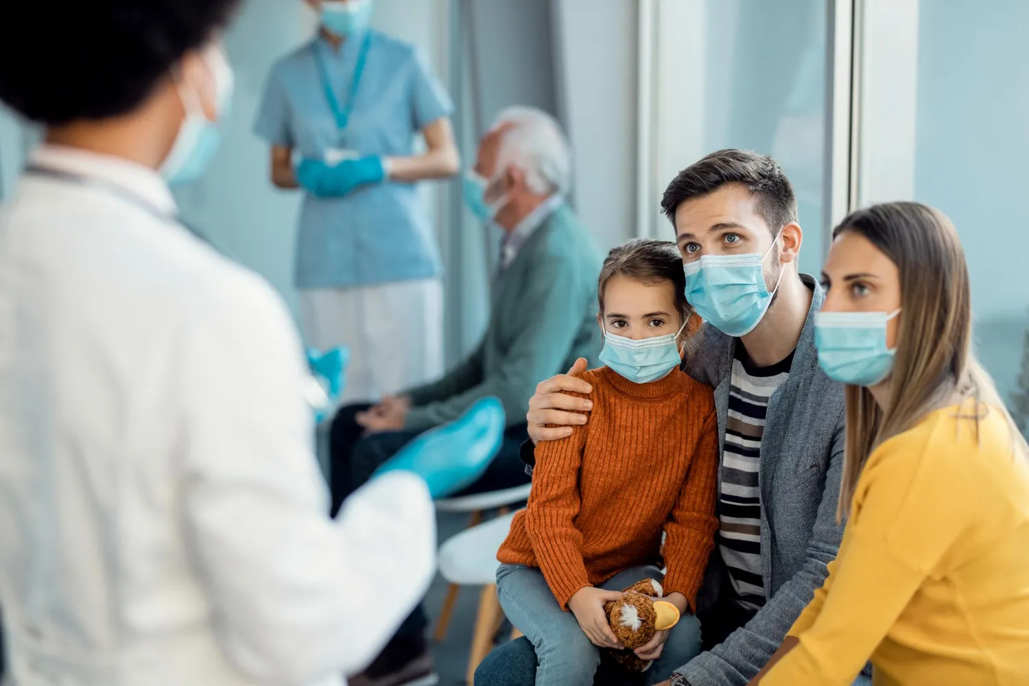 Young family with protective face masks talking to a doctor at medical clinic